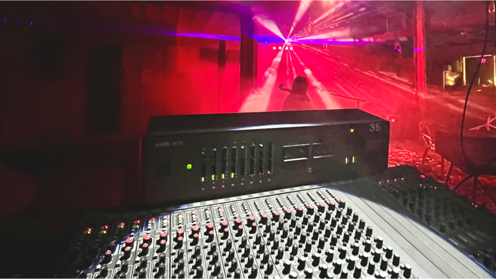 Spotlight on a large professional mixer board with smoke and accent lights in the background.