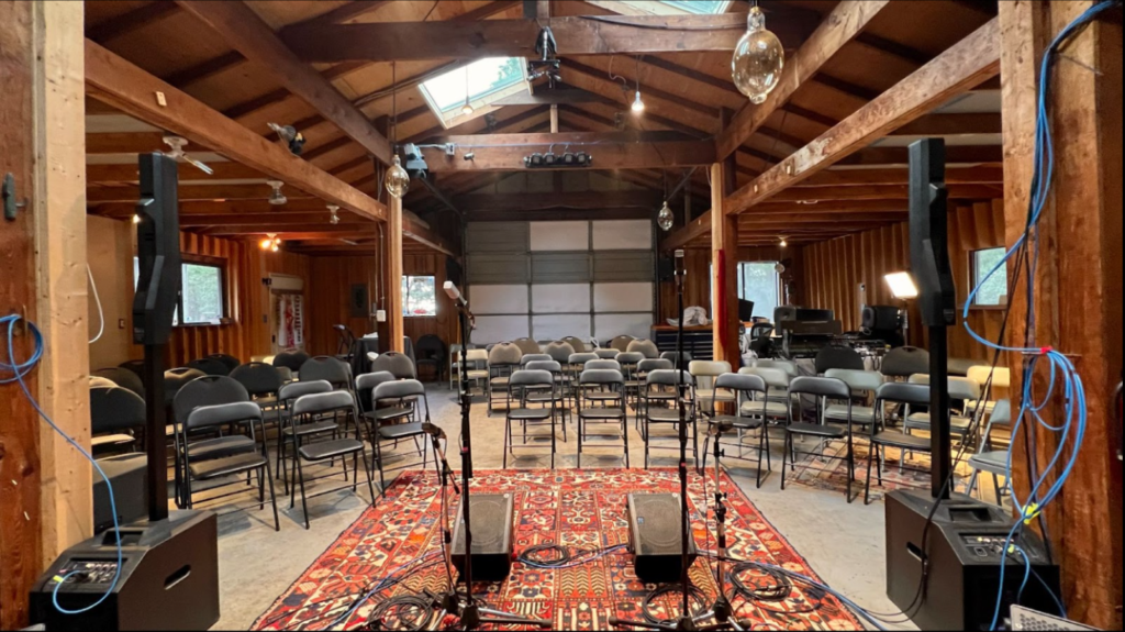 The inside of a large barn set up as a performance space with carpets, lighting, sound equipment and rows of chairs.